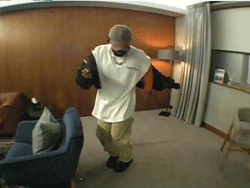 A Man In A White Shirt Is Standing In A Room GIF