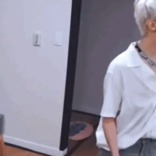 A Man In A White Shirt Is Standing In A Room Next To A Doorway . GIF