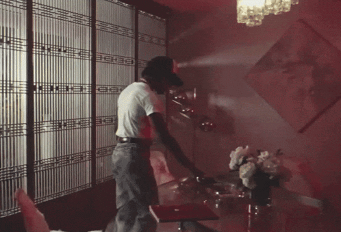 A Man In A White Shirt Is Standing In A Room With A Red Light On The Ceiling GIF