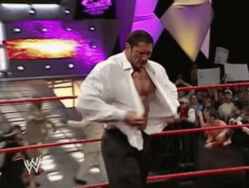 A Man In A White Shirt Is Standing In A Wrestling Ring With The Letter W On The Ring GIF