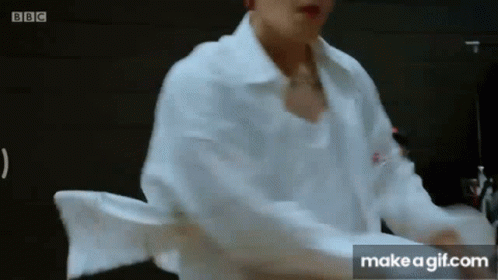 A Man In A White Shirt Is Standing In Front Of A Black Wall . GIF