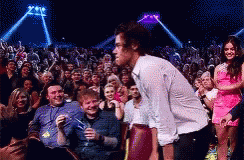 A Man In A White Shirt Is Standing In Front Of A Crowd Of People At A Concert . GIF