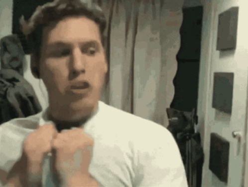 A Man In A White Shirt Is Standing In Front Of A Door GIF