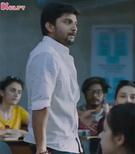 A Man In A White Shirt Is Standing In Front Of A Group Of People In A Classroom With The Word Kulfy On The Bottom GIF