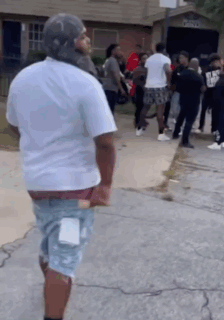 A Man In A White Shirt Is Standing In Front Of A Group Of People On The Sidewalk . GIF