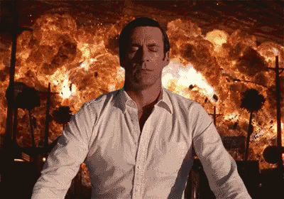 A Man In A White Shirt Is Standing In Front Of A Large Explosion GIF