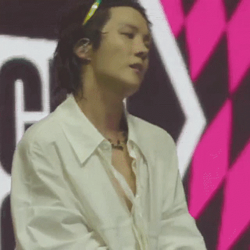 A Man In A White Shirt Is Standing In Front Of A Pink And Black Checkered Wall . GIF