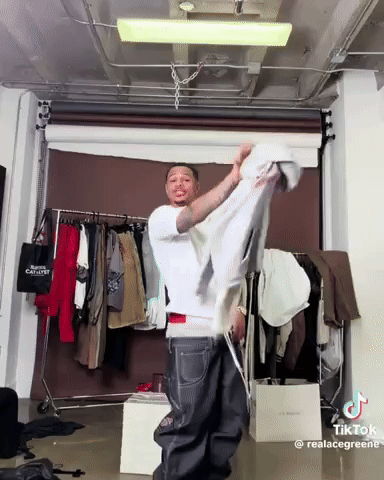 Man In White Shirt Holding Shirt In Front Of Clothes Rack GIF