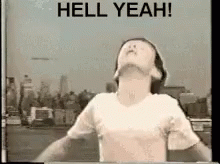 A Man In A White Shirt Is Standing In Front Of A Sign That Says Hell Yeah . GIF