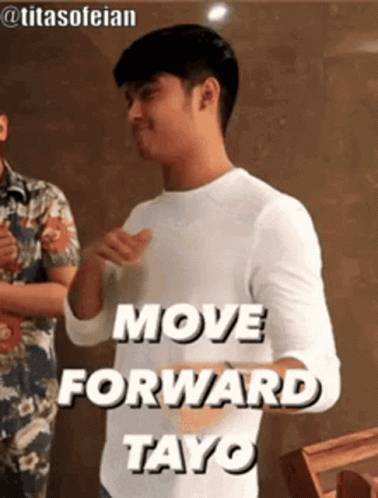 A Man In A White Shirt Is Standing In Front Of A Sign That Says `` Move Forward Tayo '' . GIF