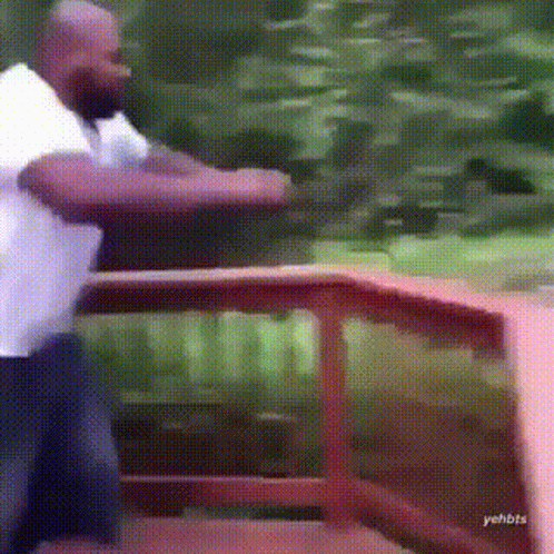 A Man In A White Shirt Is Standing In Front Of A Wooden Railing . GIF