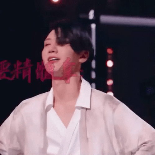 A Man In A White Shirt Is Standing On A Stage With His Hands In His Pockets . GIF