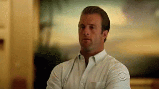 A Man In A White Shirt Is Standing With His Arms Crossed And Looking At The Camera . GIF