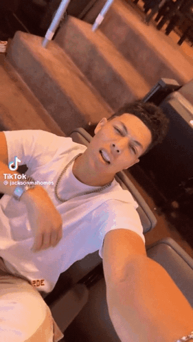A Man In A White Shirt Is Taking A Selfie While Wearing A Gold Chain Around His Neck . GIF
