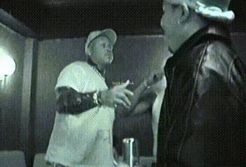 A Man In A White Shirt Is Talking To Another Man GIF