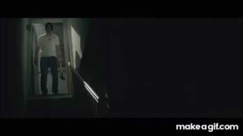 a man in a white shirt is walking down a set of stairs with a knife in his hand .