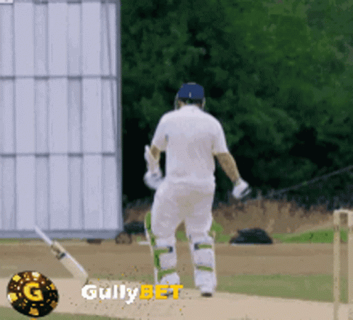 A Man In A White Shirt Is Walking On A Cricket Field With Gullybet Written On The Bottom GIF