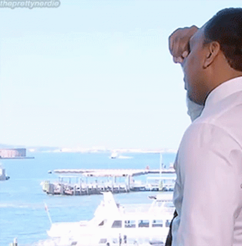 A Man In A White Shirt Looks Out A Window At The Water GIF
