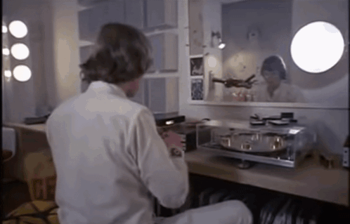 A Man In A White Shirt Sits At A Table In Front Of A Mirror With The Word Gf On It GIF