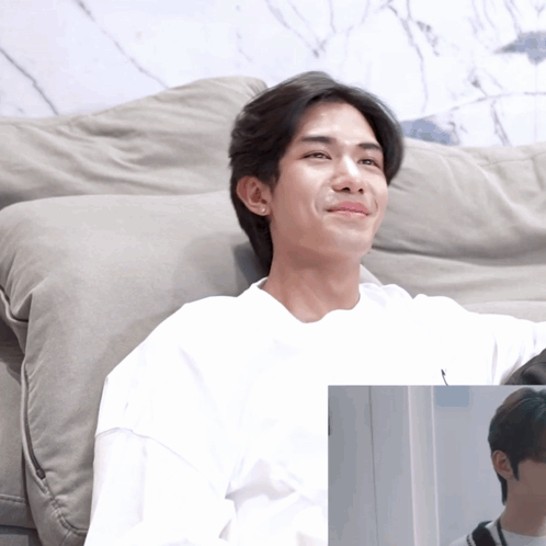 A Man In A White Shirt Sits On A Grey Couch GIF