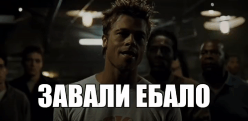 A Man In A White Shirt Stands In A Dark Room With The Words " Завали Ебалo " Above Him GIF
