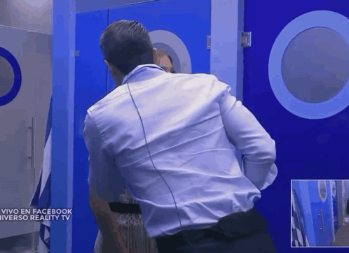 A Man In A White Shirt Stands In Front Of A Blue Door That Says Vivo En Facebook Universo Reality Tv GIF
