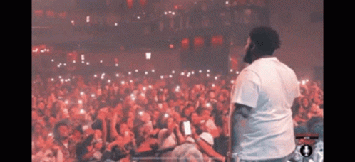 A Man In A White Shirt Stands In Front Of A Large Crowd GIF