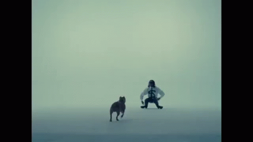 A Man In A White Shirt With A Cross On It Stands Next To A Dog GIF