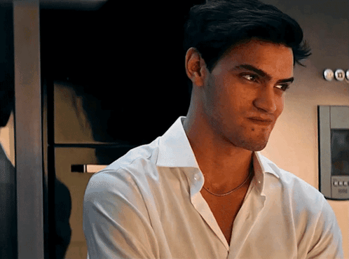 A Man In A White Shirt With A Necklace Around His Neck Looks At The Camera GIF