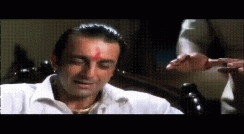 A Man In A White Shirt With A Red Spot On His Forehead Is Sitting On A Chair . GIF