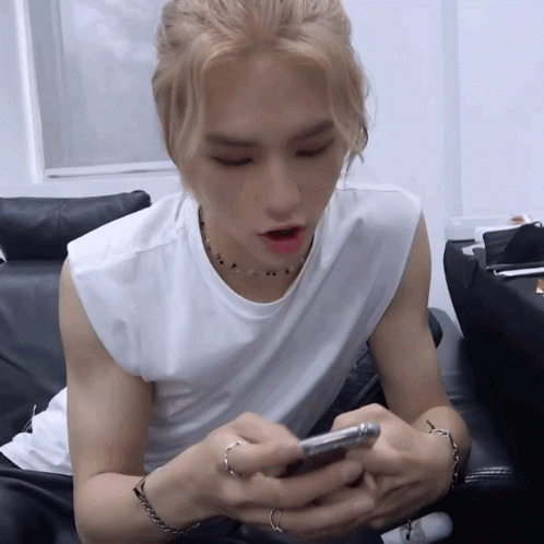 A Man In A White Sleeveless Shirt Is Looking At His Cell Phone GIF