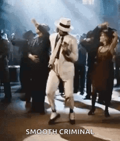 A Man In A White Suit And Hat Is Dancing In Front Of A Crowd At A Party . GIF