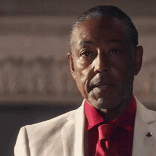 A Man In A White Suit And Red Tie Is Looking At The Camera GIF