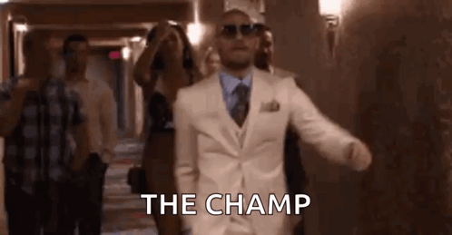 A Man In A White Suit And Sunglasses Is Walking Down A Hallway With A Group Of People . GIF