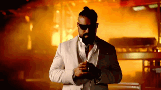 A Man In A White Suit And Sunglasses Stands In Front Of A Fire GIF
