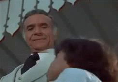 A Man In A White Suit And Tie Is Kissing A Woman . GIF