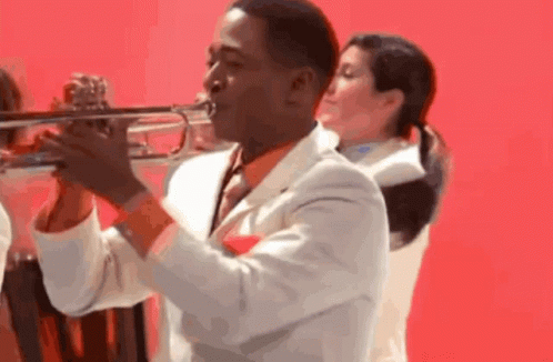 A Man In A White Suit And Tie Is Playing A Trumpet GIF