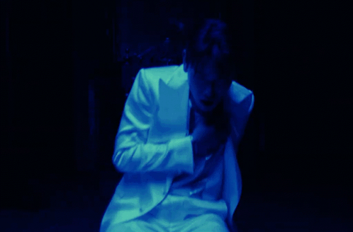 A Man In A White Suit Covering His Face With His Hand GIF
