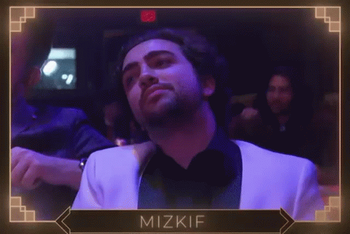 A Man In A White Suit Is Dancing In A Dark Room With The Name Mizkif On The Bottom Right GIF