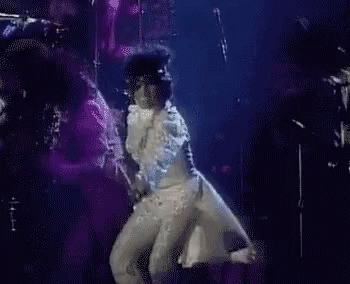 A Man In A White Suit Is Dancing On A Stage . GIF