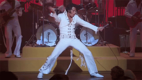 A Man In A White Suit Is Holding A Microphone And Dancing On Stage GIF