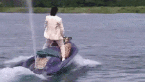A Man In A White Suit Is Riding A Jet Ski On A Lake . GIF