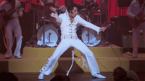 A Man In A White Suit Is Singing Into A Microphone On A Stage GIF