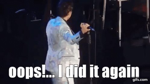 A Man In A White Suit Is Singing Into A Microphone On A Stage And Says Oops ! I Did It Again . GIF