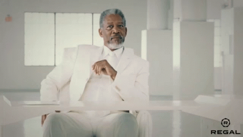 A Man In A White Suit Is Sitting At A Table With Regal Written On The Bottom GIF