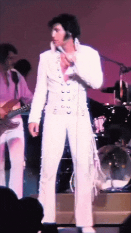 A Man In A White Suit Is Standing In Front Of A Microphone GIF
