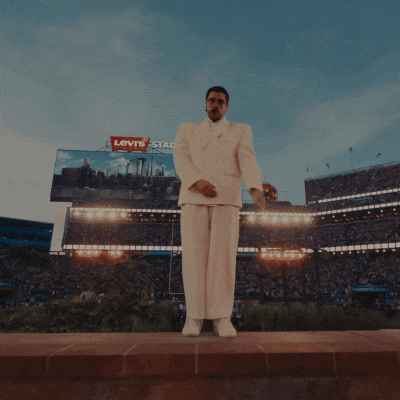 A Man In A White Suit Stands In A Crowd Of People GIF