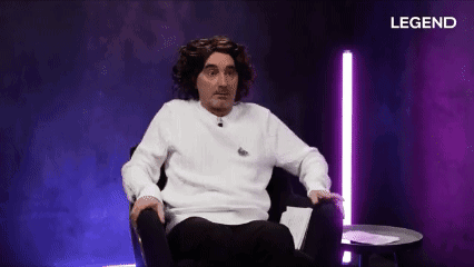 A Man In A White Sweater Is Sitting In A Chair In Front Of A Purple Background With Legend Written On It GIF