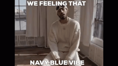 A Man In A White Sweater Is Sitting In Front Of A Window With The Caption " We Feeling That Navy Blue Vibe " GIF