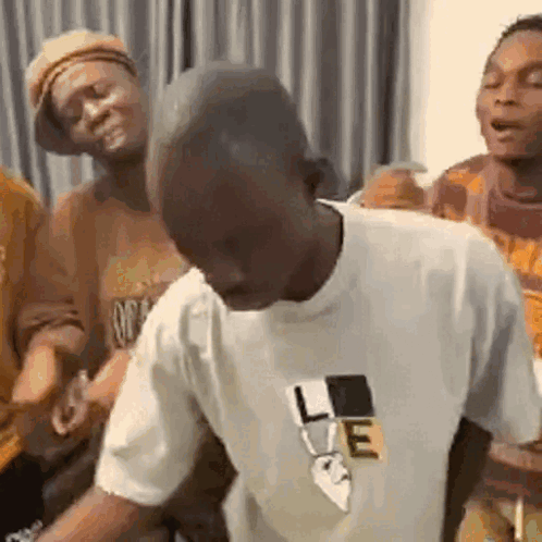 A Man In A White T-Shirt Is Dancing In A Room With Other People . GIF